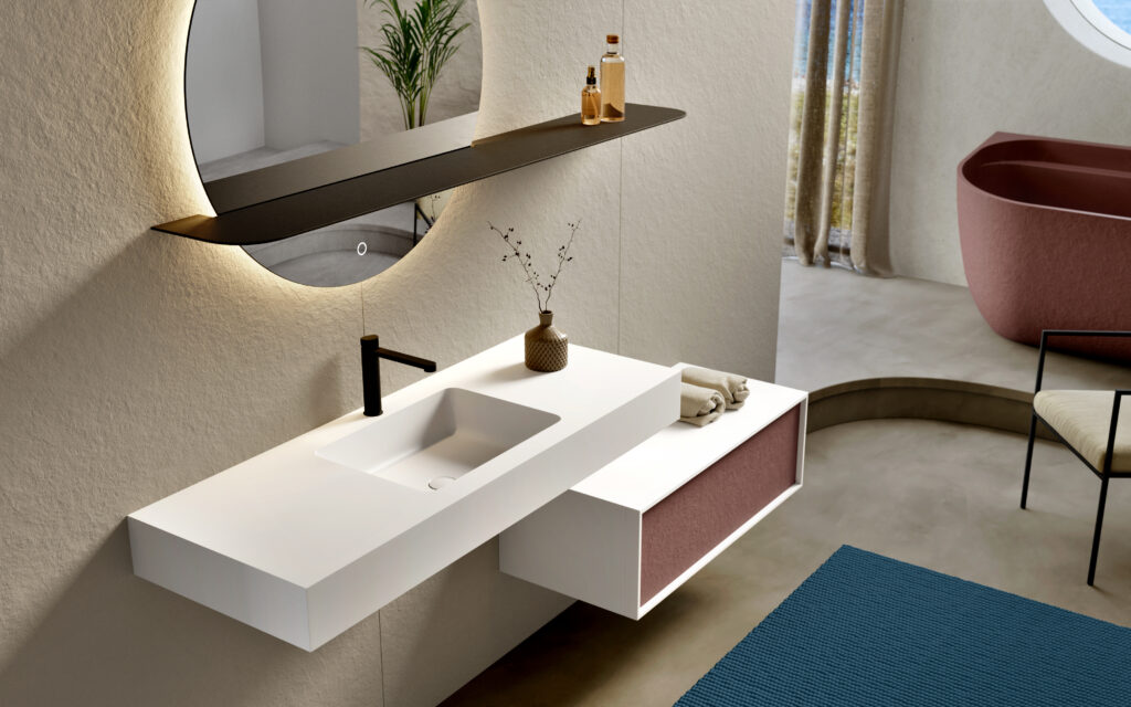 Modern bathroom with a minimalist white sink, round backlit mirror, and sleek black faucet. A coral bathtub and neutral tones create a calm atmosphere.