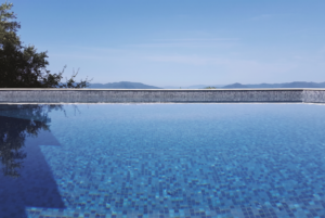 Infinity pool with a clear blue sky and distant mountains in the background. Tranquil and serene atmosphere with lush greenery on the left.