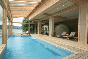 A spacious indoor pool surrounded by wooden flooring and a wooden ceiling, creating a warm and inviting atmosphere.