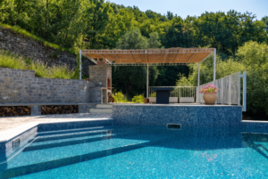 Luxury backyard swimming pool lined with Classic Deep Swimming mosaic tiles, featuring an attached spa with a small waterfall feature.