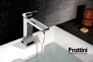 Luxury minimalist bathroom featuring a white countertop washbasin on a dark wooden floating shelf with elegant brass fittings by Frattini.