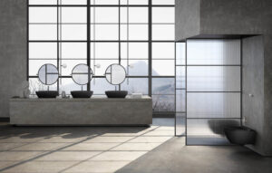 Industrial style bathroom with large grid windows, featuring a long stone console with three matte black GSI Color Elements washbasins and round mirrors.