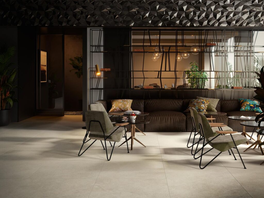 Modern lounge interior featuring dark geometric walls, green chairs, and a brown sectional sofa with colorful cushions.