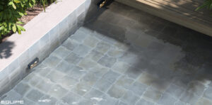 Close-up of a sunken spa or pool steps with Sea Matt grey-blue tiles, featuring integrated LED lighting and a wooden bench.